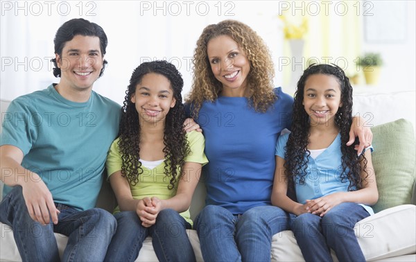 Portrait of parents with daughters (10-13) sitting on sofa.
