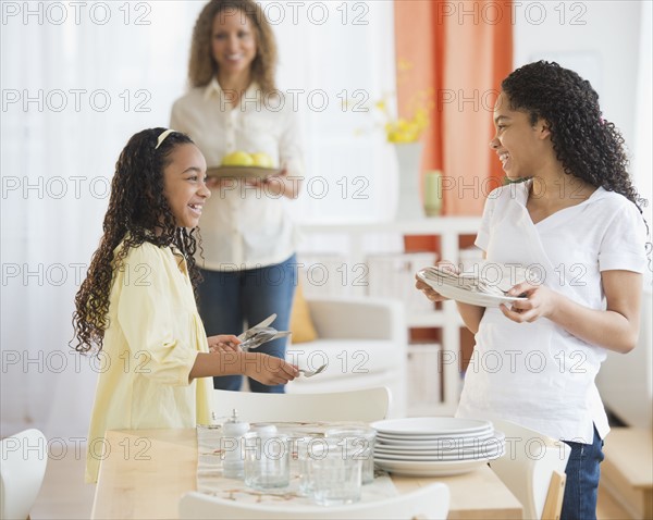 Mother with daughters (10-13) setting table.