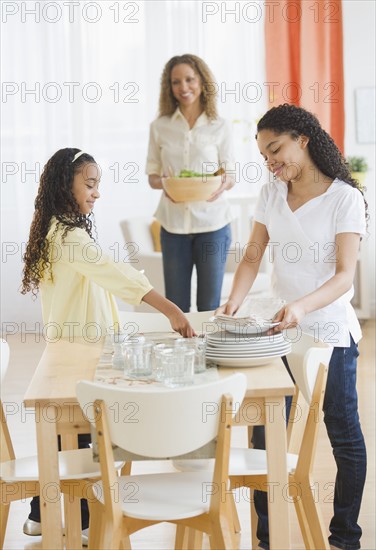 Mother with daughters (10-13) setting table.