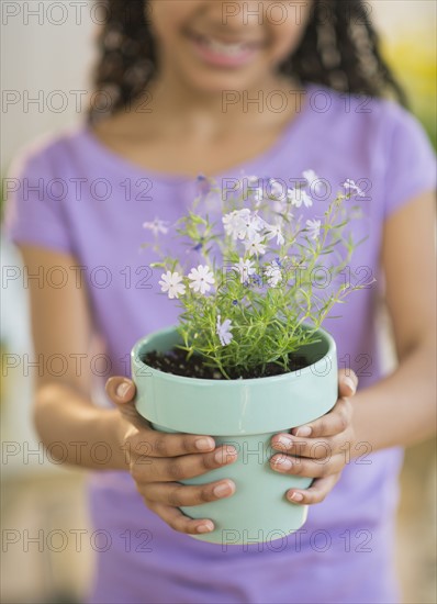 Girl (10-11) holding potted flower.