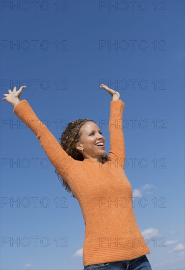 Mature woman with arms raised towards blue sky.