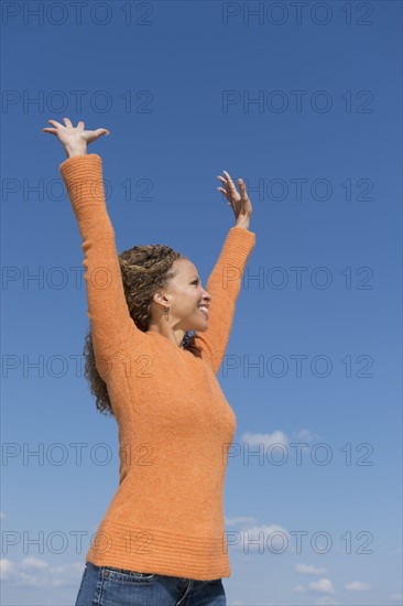 Mature woman with arms raised towards blue sky.