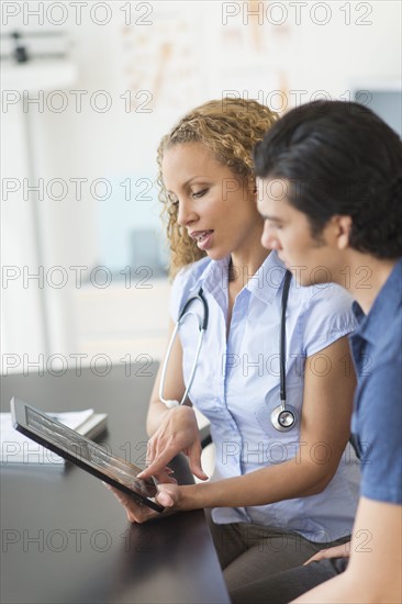Doctor and patient talking in clinic using tablet pc.