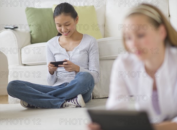 Two girls (14-17) relaxing at home using digital devices.