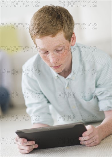 Boy (16-17) lying on floor using tablet pc.