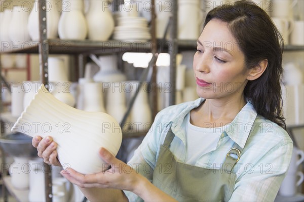 Woman holding vase in pottery warehouse.
