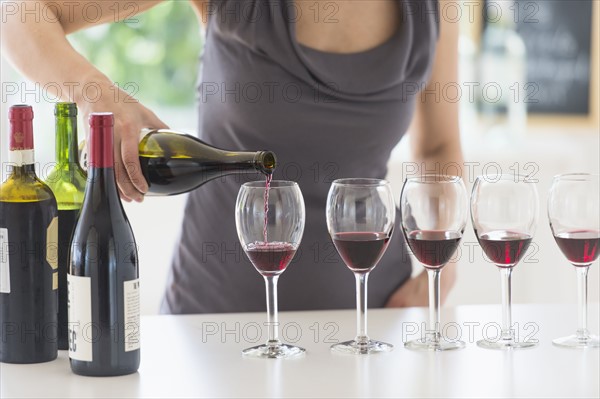 Woman purring red wine into wine glasses.