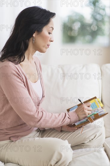 Woman sitting on sofa and writing in personal organizer.