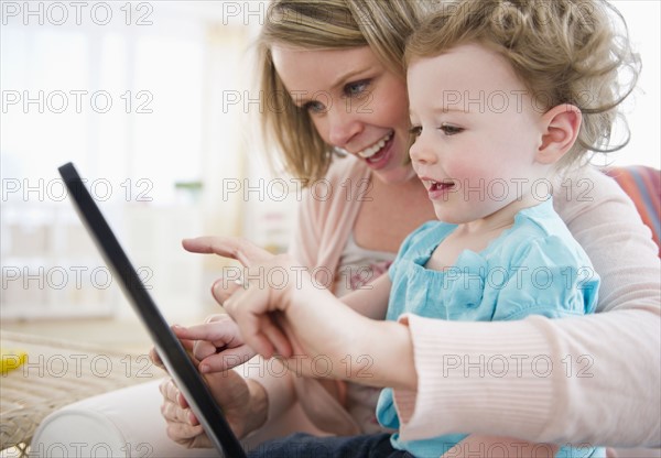 Mother with daughter (-11 months) using digital tablet at home.
Photo : Jamie Grill