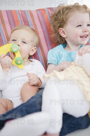 Brother and sister (2-3, 6-11 months) sitting on sofa. 
Photo : Jamie Grill