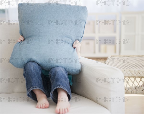 Girl (2-3) sitting on sofa hiding behind pillow. 
Photo : Jamie Grill
