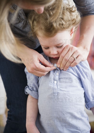 Mother buttoning daughter's (2-3) shirt. 
Photo : Jamie Grill