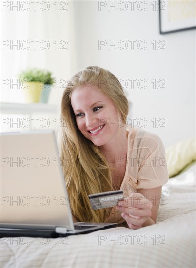 Woman online shopping while lying on bed. 
Photo : Jamie Grill