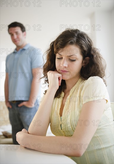 Sad woman sitting at table, man in background. 
Photo : Jamie Grill