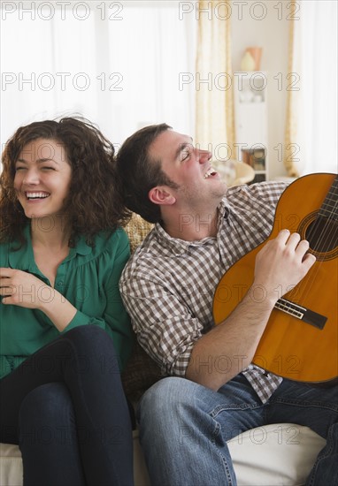 Couple sitting on sofa, man playing guitar. 
Photo : Jamie Grill