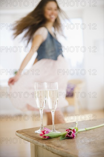 Champagne flutes on table, woman dancing in background. 
Photo : Jamie Grill