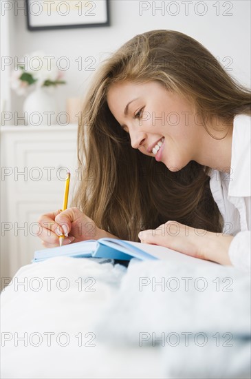 Woman lying on bed and writing diary. 
Photo : Jamie Grill