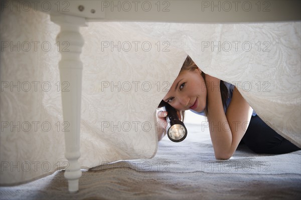 Woman with flashlight looking under bed. 
Photo : Jamie Grill