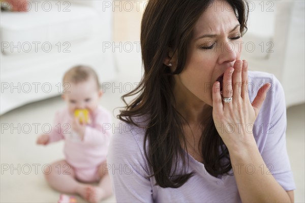 Tired woman yawning, baby daughter (6-11 months) in background. 
Photo: Jamie Grill