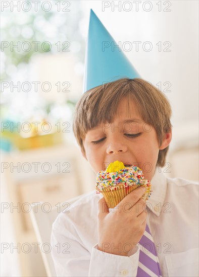Portrait of boy (10-11 years) in party hat eating cupcake. 
Photo: Daniel Grill