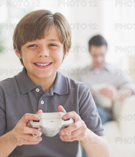 Boy (10-11 years) playing video game with father sitting in background. 
Photo : Daniel Grill