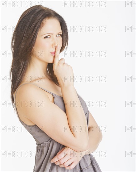 Portrait of young woman with finger on lips, studio shot. 
Photo : Daniel Grill