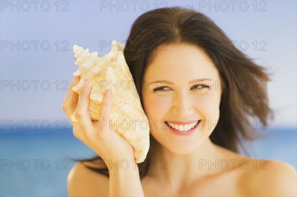 Portrait of young woman listening to seashell, studio shot. 
Photo: Daniel Grill