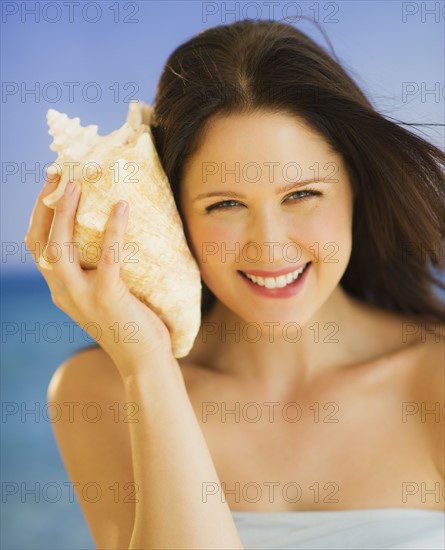 Portrait of young woman listening to seashell, studio shot. 
Photo : Daniel Grill