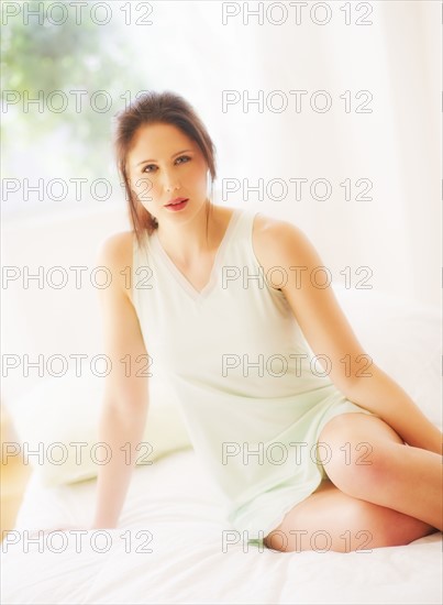 Portrait of young woman sitting on bed. 
Photo : Daniel Grill