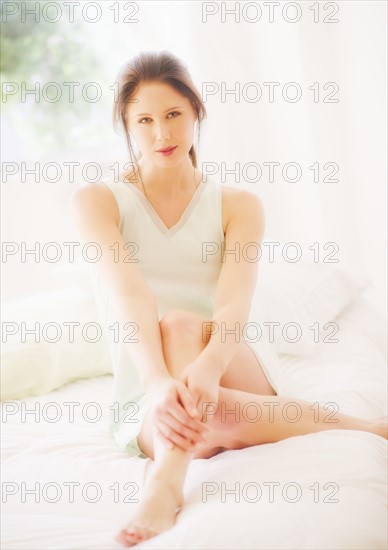 Portrait of young woman sitting on bed. 
Photo : Daniel Grill