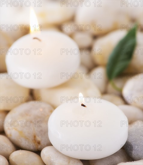 Close up of tea lights and green leaf on pebble stones, studio shot. 
Photo : Daniel Grill