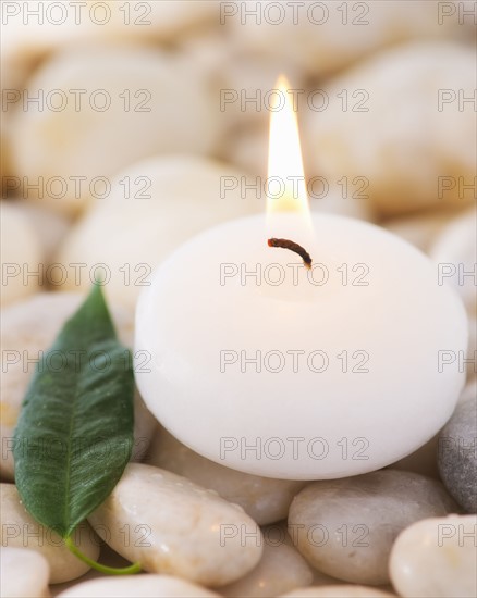 Close up of tea light and green leaf on pebble stones, studio shot. 
Photo : Daniel Grill