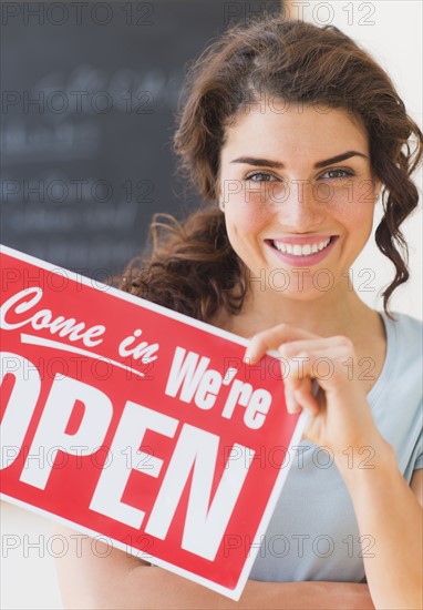 Portrait of smiling waitress showing open sign. 
Photo: Daniel Grill