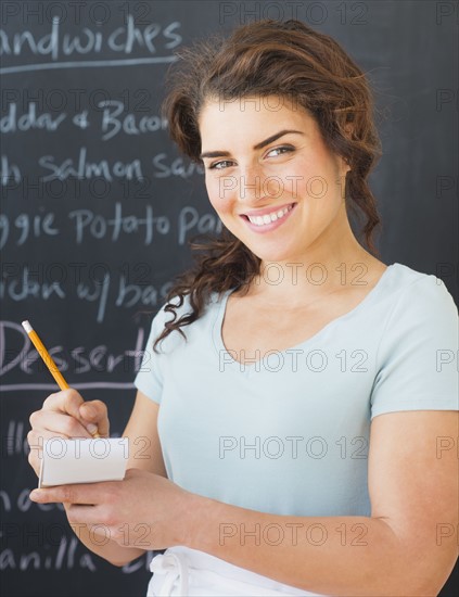 Portrait of smiling waitress against blackboard with menu. 
Photo : Daniel Grill