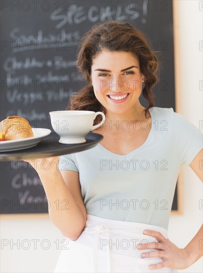 Portrait of smiling waitress with tray against blackboard with menu. 
Photo : Daniel Grill