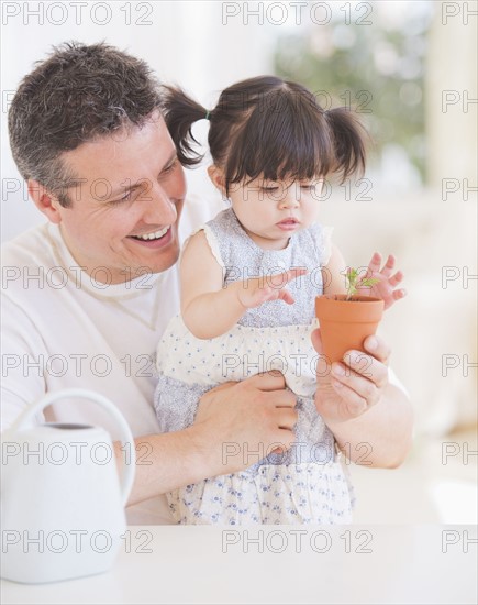 Baby girl (12-17 months) with father watching seedling in pot. 
Photo : Daniel Grill