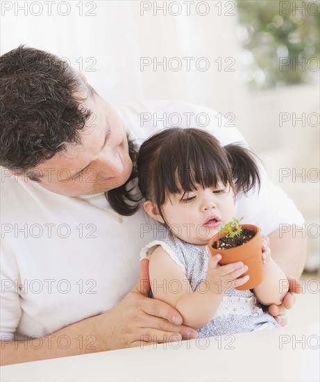 Baby girl (12-17 months) with father watching seedling in pot. 
Photo : Daniel Grill