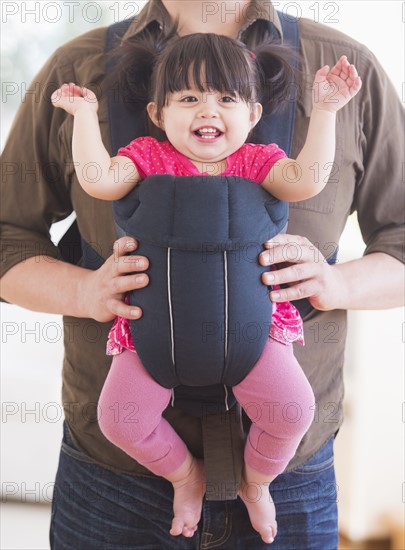 Baby girl (12-17 months) in baby carrier held by her father. 
Photo : Daniel Grill