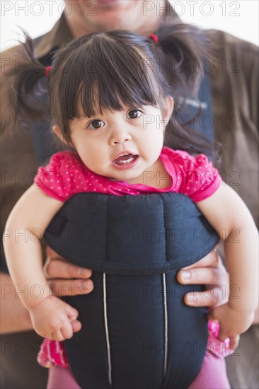 Baby girl (12-17 months) in baby carrier held by her father. 
Photo : Daniel Grill