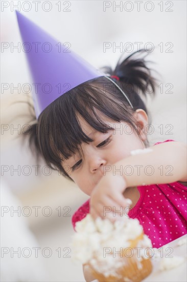 Portrait of baby girl (12-17 months) in party hat eating cupcake.
Photo : Daniel Grill