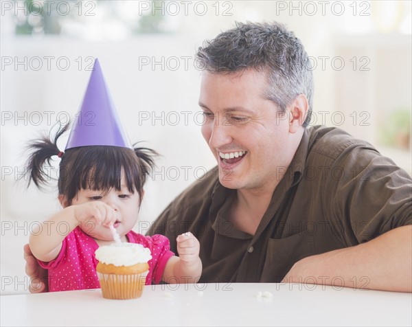 Portrait of father and baby girl (12-17 months) in party hat eating cupcake.
Photo : Daniel Grill