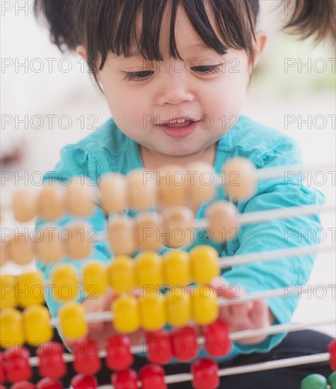 Portrait of baby girl (12-17 months) playing with abacus. 
Photo: Daniel Grill