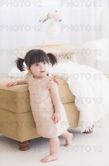 Portrait of baby girl (12-17 months) standing near sofa. 
Photo : Daniel Grill