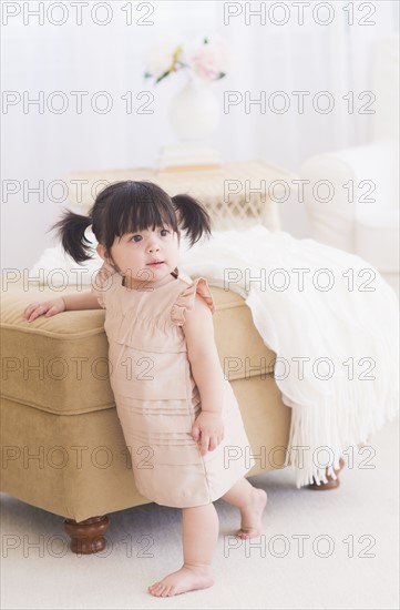 Portrait of baby girl (12-17 months) standing near sofa.
Photo : Daniel Grill
