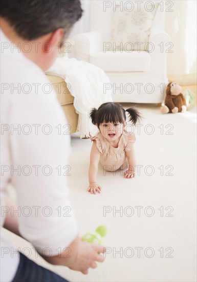 Father encouraging baby daughter (12-17 months) to crawl. 
Photo : Daniel Grill