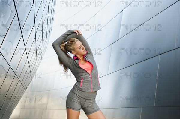 USA, California, Los Angeles, Young woman stretching near modern building.