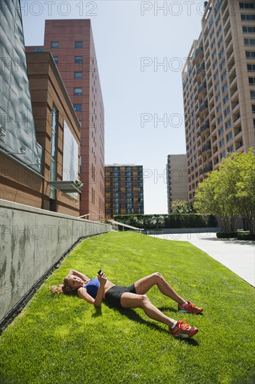 USA, California, Los Angeles, Young woman listening to music while lying on grass after training.