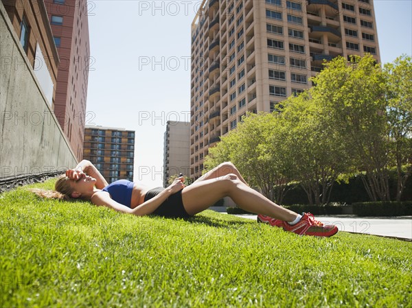 USA, California, Los Angeles, Young woman listening to music while lying on grass after training.