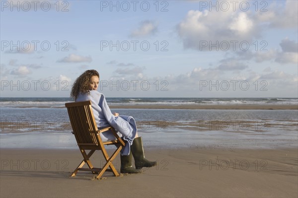 France, Pas-de-Calais, Escalles, Young woman sitting on chair on empty beach. 
Photo : Jan Scherders