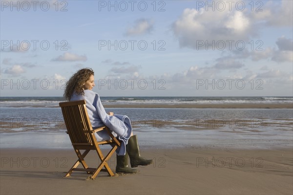 France, Pas-de-Calais, Escalles, Young woman sitting on chair on empty beach. 
Photo: Jan Scherders